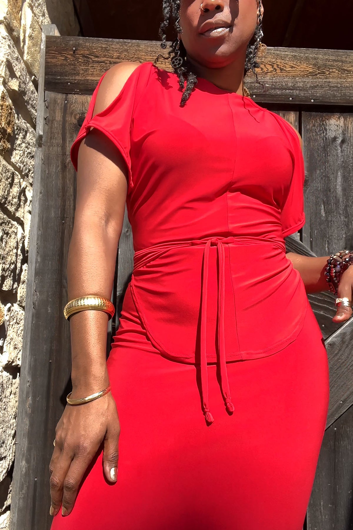 Woman wearing a red dress standing against a wooden and stone wall.