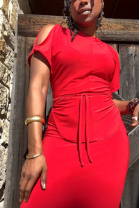 Woman wearing a red dress standing against a wooden and stone wall.